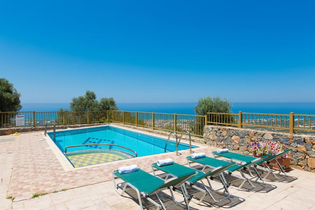 uma piscina com mesas e cadeiras e o oceano ao fundo em Maroulas Villas Ioanna & Stavros, stunning views, By ThinkVilla em Maroulás