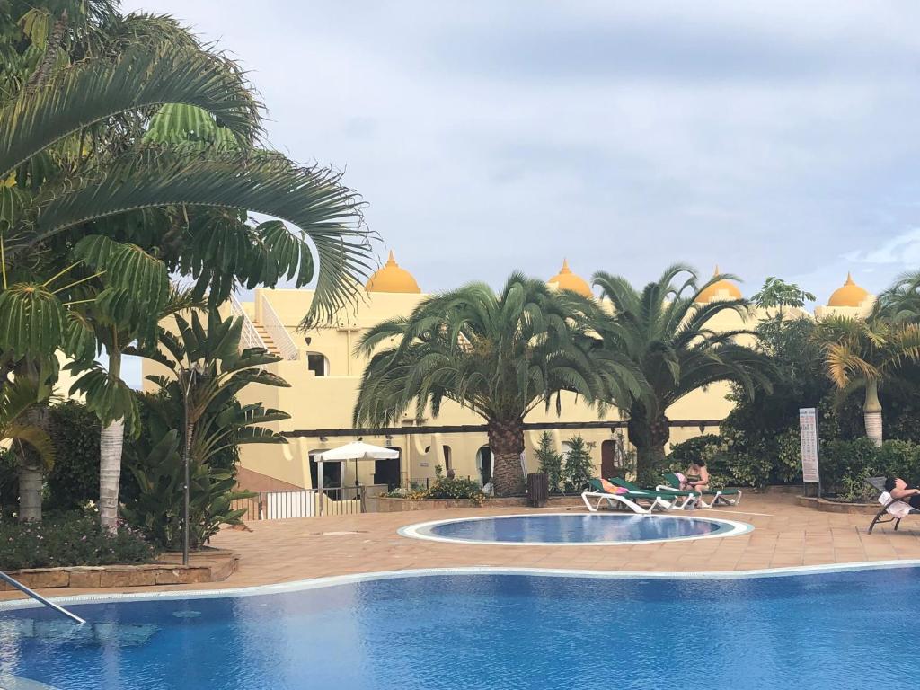 a swimming pool with palm trees and a building at 60 El Sultan, 20 Pedroy Guy Vandaele in Corralejo