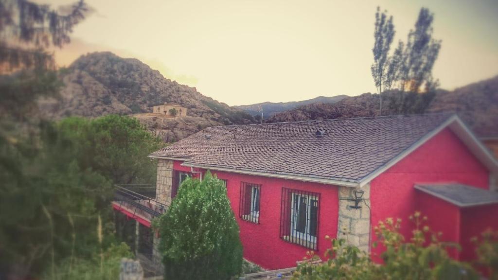 uma casa vermelha com uma montanha ao fundo em Casa Piedra Libre em Manzanares el Real