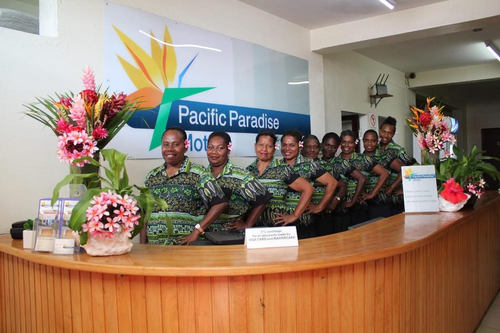 Un groupe d'hommes en uniformes verts se tenant derrière un comptoir dans l'établissement Pacific Paradise Motel, à Port Vila