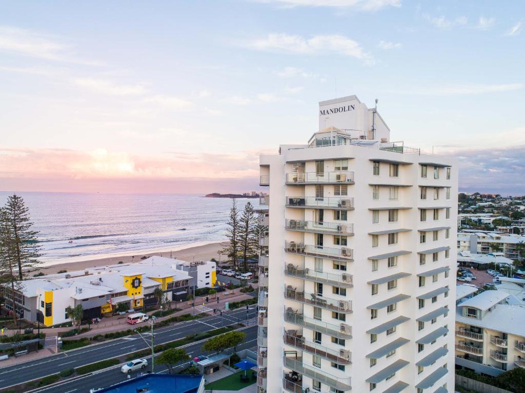 een hoog wit gebouw naast een strand bij Mandolin Resort in Alexandra Headland