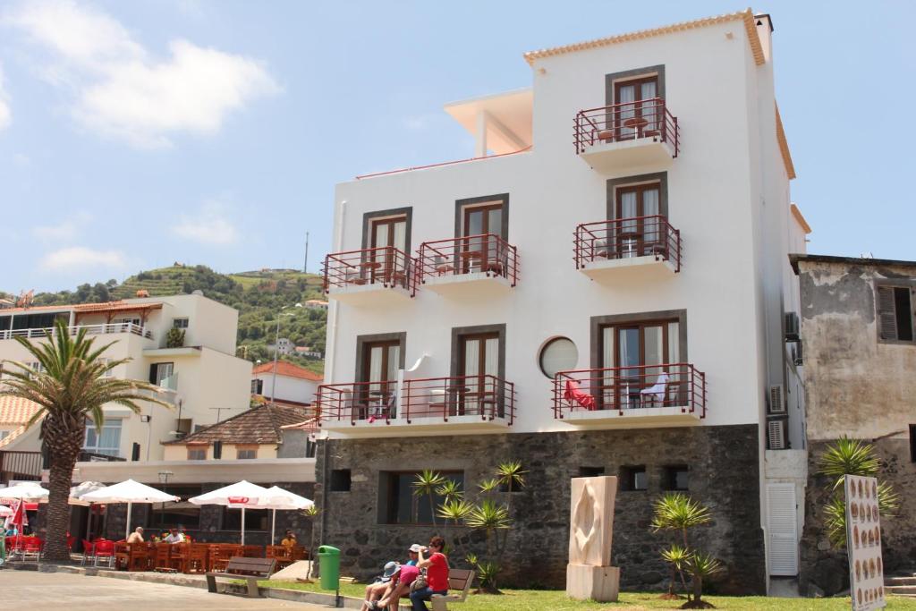 a building with a balcony and a patio area with tables and chairs at Hotel Vila Bela in Porto da Cruz