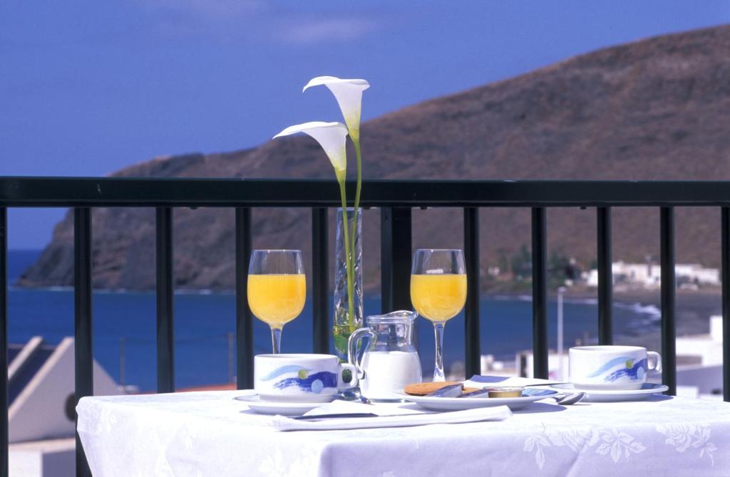 a table with two glasses of wine and a flower at Cala Apartamentos in Giniginámar