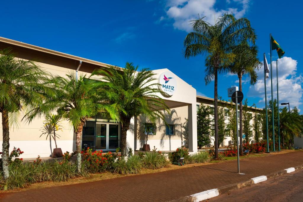 a building with palm trees in front of a street at Matiz Barão Geraldo Express Hotel in Campinas