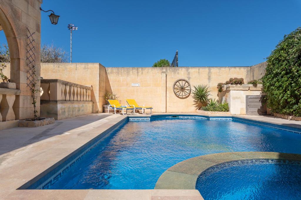 a swimming pool with two chairs in a backyard at Mood Farmhouse Mythology in Għarb