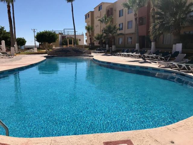 einen großen blauen Pool mit Stühlen und Palmen in der Unterkunft Condo de Cortez in Puerto Peñasco