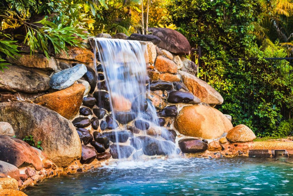 a waterfall in a stone wall with a pool of water at Malanda Lodge in Malanda