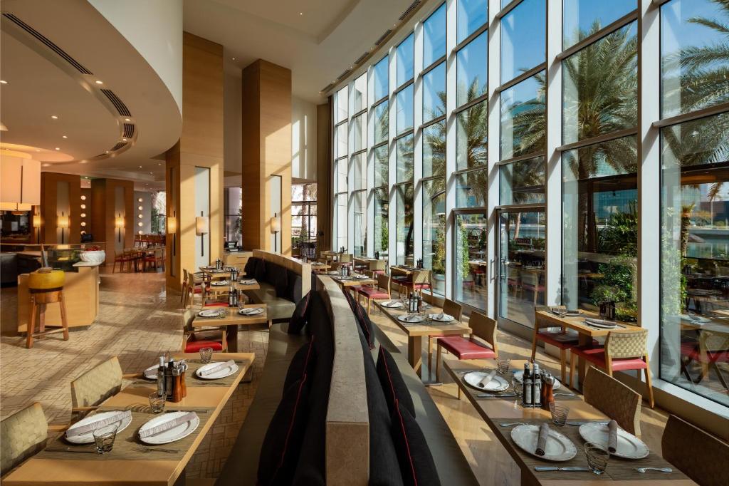 a restaurant with tables and chairs and large windows at Beach Rotana - Abu Dhabi in Abu Dhabi