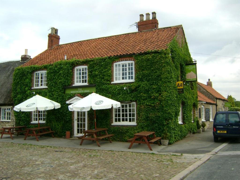 a green building with tables and umbrellas in front of it at Wentworth arms in Malton