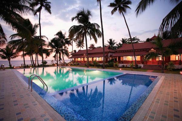 - une piscine bordée de palmiers en face d'un bâtiment dans l'établissement Cocobay Resort Kumarakom, à Kumarakom
