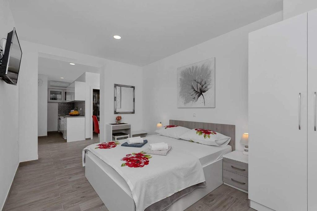 a white bedroom with a large bed with red flowers on it at Apartman-Studio Meri in Makarska