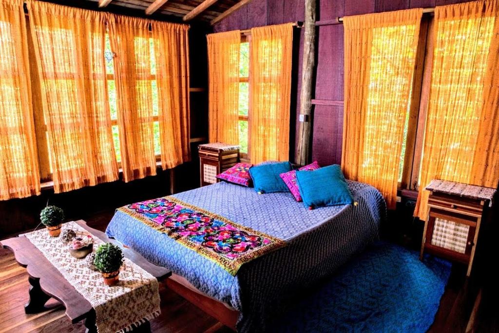 a bedroom with a bed and two tables and windows at Chalé Solar no Matutu in Aiuruoca