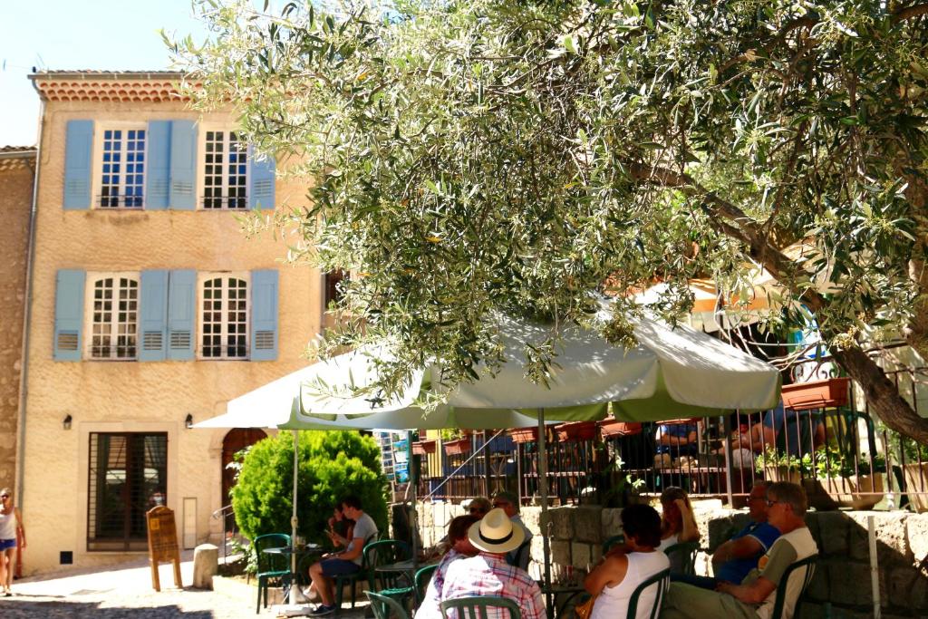 um grupo de pessoas sentadas sob um guarda-chuva em frente a um edifício em La Bonne Etoile - The Good Star em Moustiers-Sainte-Marie