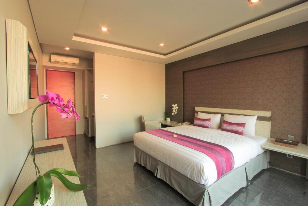 a bedroom with a large white bed with pink pillows at Transera Kamini Legian Hotel in Legian