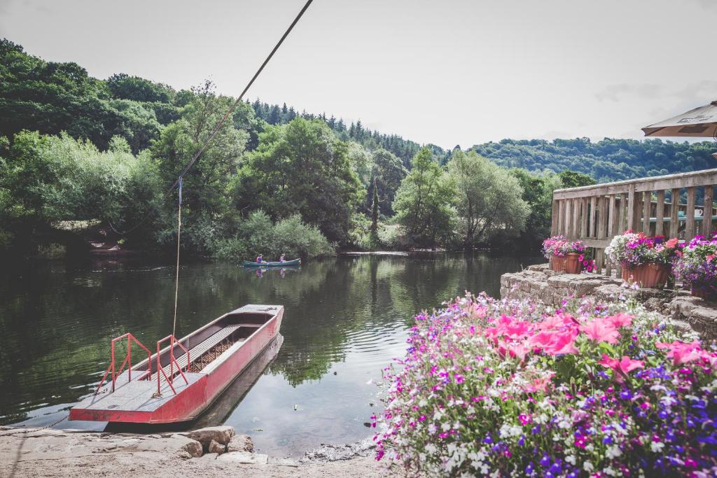 um barco sentado na água ao lado de algumas flores em Ye Old Ferrie Inn em Symonds Yat