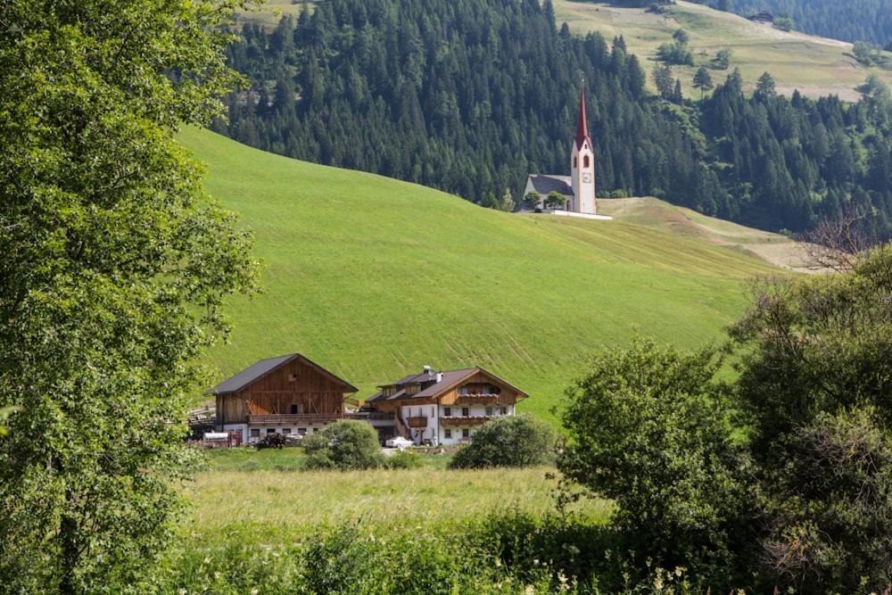 ein Haus auf einem grünen Hügel mit einem Uhrturm in der Unterkunft Parggenhof in Innichen