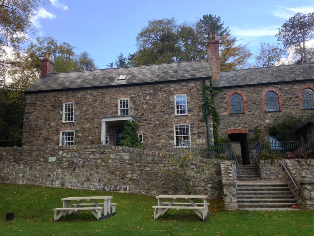- un bâtiment en pierre avec deux tables de pique-nique devant dans l'établissement The Farmhouse at Bodnant Welsh Food, à Conwy