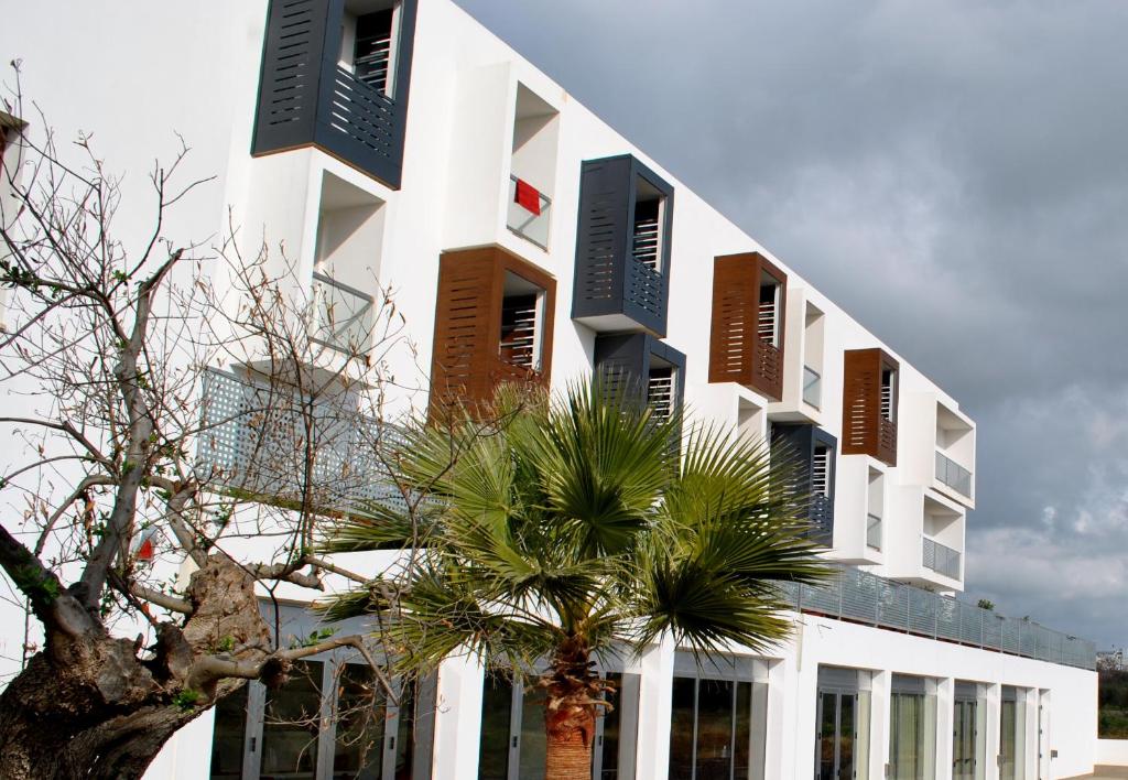 a white building with brown shutters and a palm tree at Althea Palace Hotel in Castelvetrano Selinunte