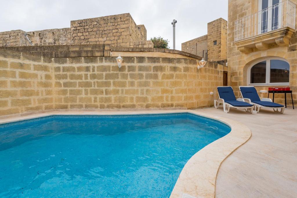 a swimming pool with two blue chairs next to a brick wall at Entire Villa - Gemini Farmhouse, Nadur Gozo in Nadur