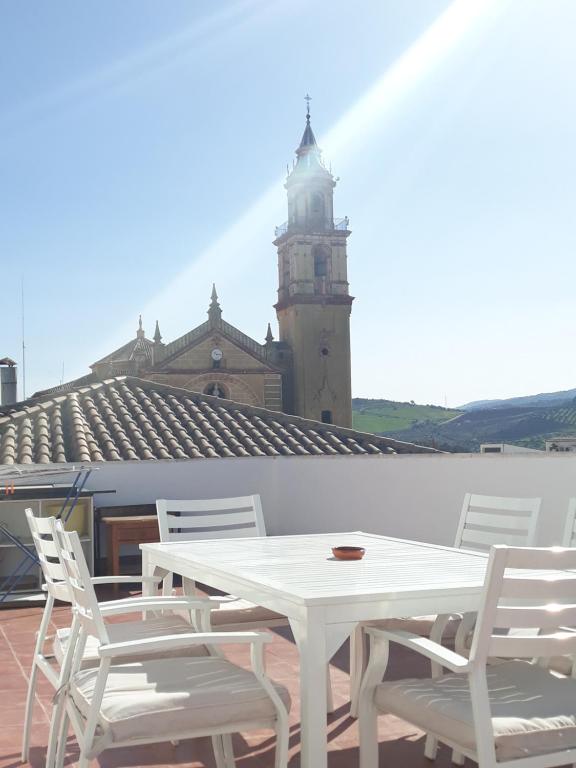 una mesa blanca y sillas en un techo con una torre de reloj en ATICO-PLAZA, en Algodonales