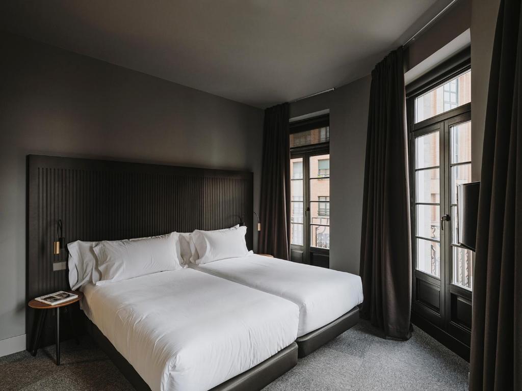 a bedroom with a large white bed and two windows at El Môderne Hotel in Gijón