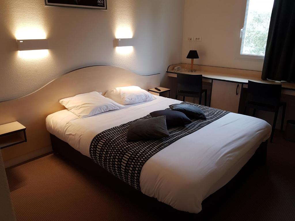 um quarto com uma cama grande com lençóis brancos e almofadas em ACE Hôtel Vendée Saint Hermine em Sainte-Hermine