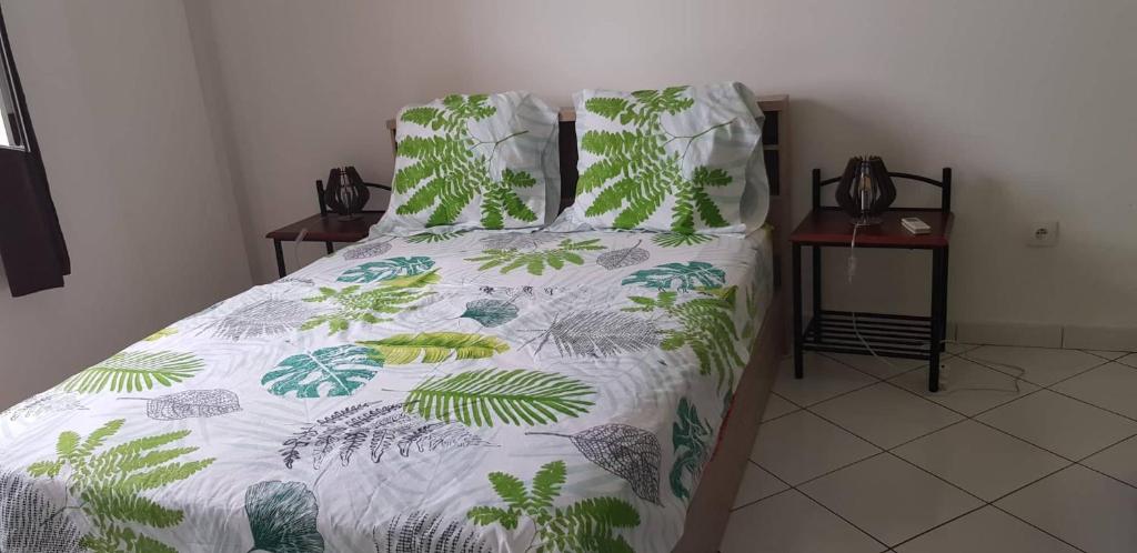 1 cama con edredón blanco con hojas verdes en Au Franciscea , appartement T3, en Saint-Louis