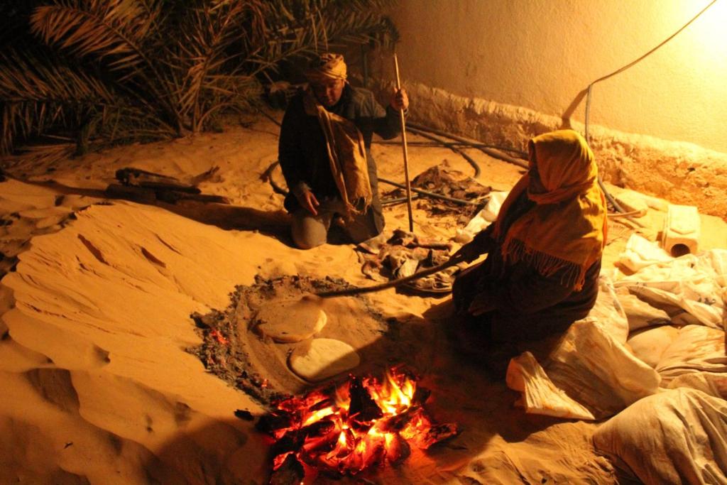 dos personas de pie alrededor de un fuego en la arena en Maison Proche De Désert Douz, en Douz