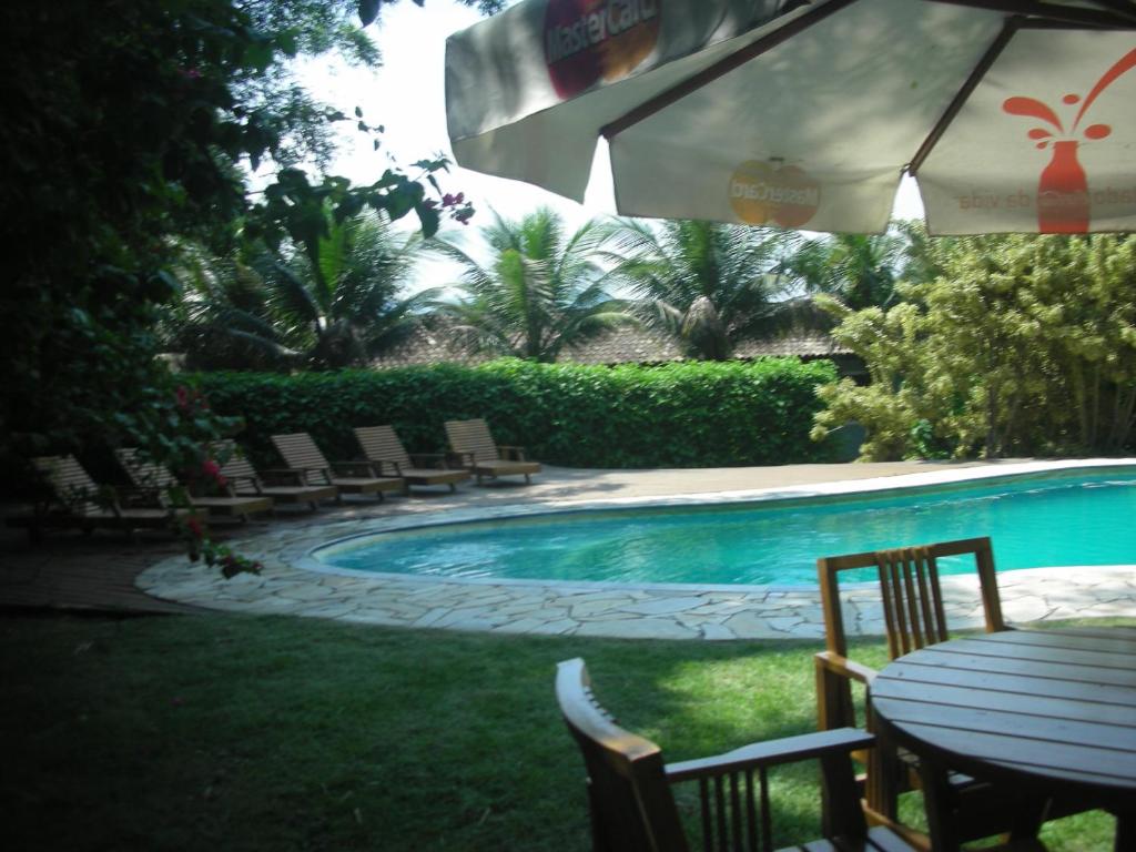 a swimming pool with chairs and a table and an umbrella at Pousada das Maritacas in Ilhabela