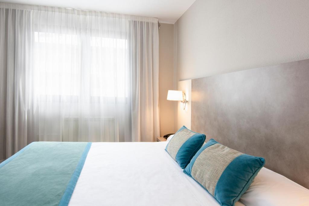 a bedroom with a bed with blue pillows and a window at Hotel & Spa Real Jaca in Jaca