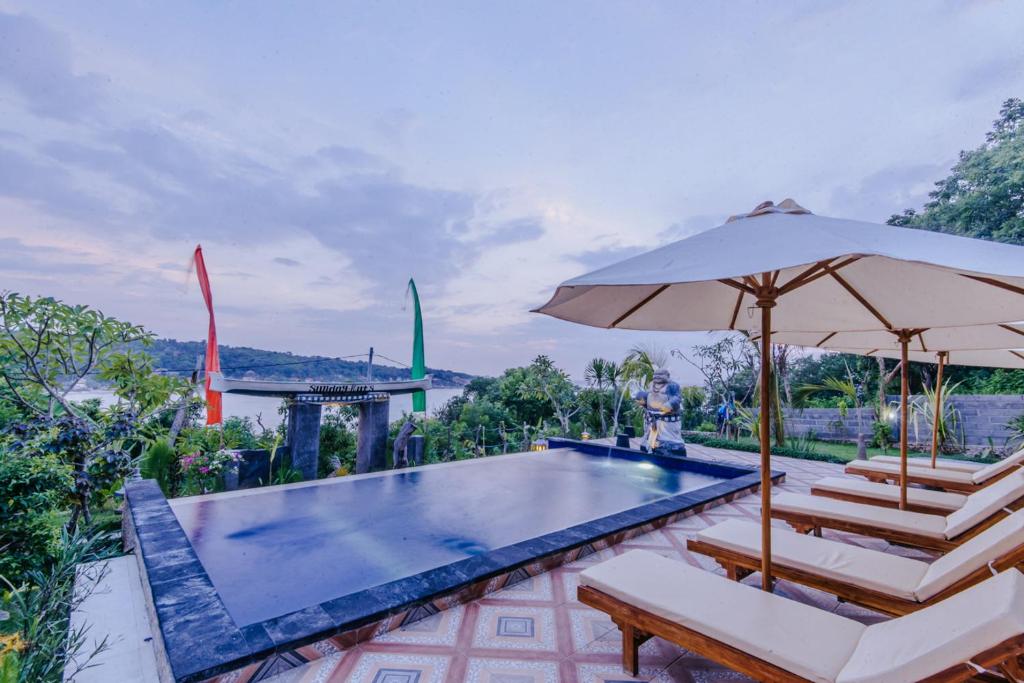 a swimming pool with two chairs and an umbrella at Sunday Huts Lembongan in Nusa Lembongan