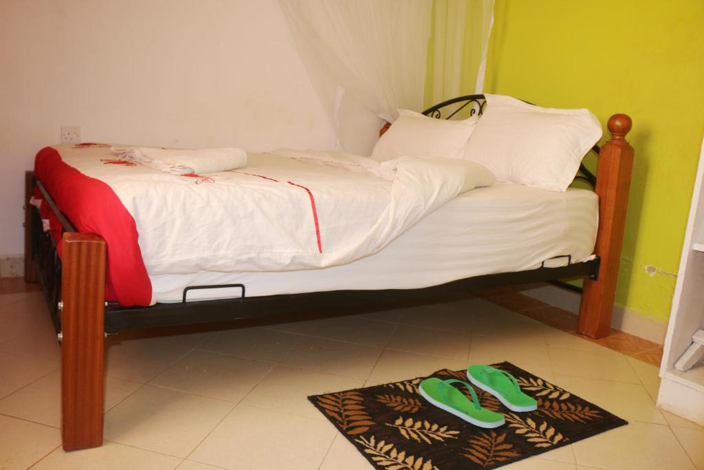 een klein bed met groene slippers op de vloer bij Preston Pointe Resort in Kisii