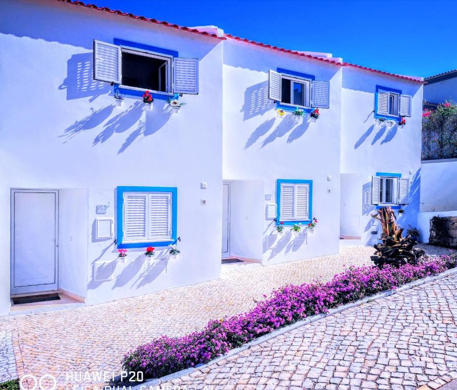 ein weißes Gebäude mit blauen Fenstern und lila Blumen in der Unterkunft 3 Villas - Praia da Falesia in Albufeira