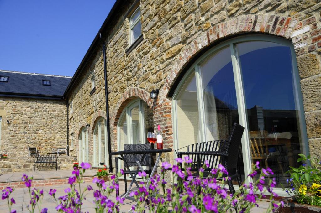 a brick building with a table and chairs and purple flowers at Riding Farm Cottages in Gateshead