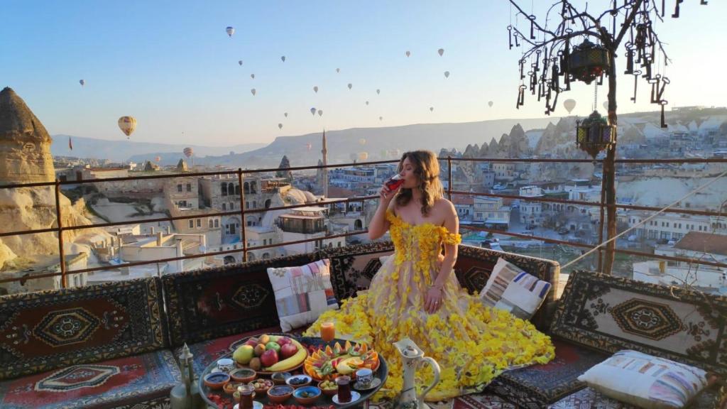 una mujer con un vestido amarillo sentada en un balcón en Antique Terrace Cave Suites, en Göreme