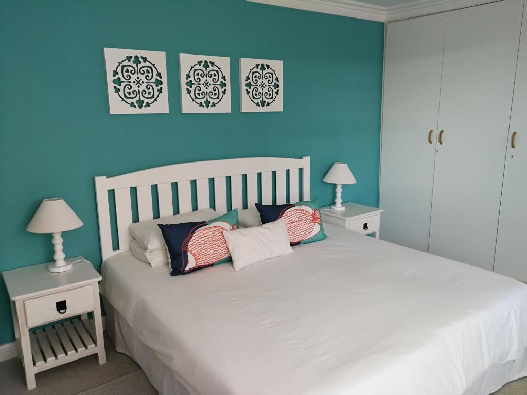 a bedroom with a white bed with blue walls and two tables at Sit-en-Kyk in Hermanus