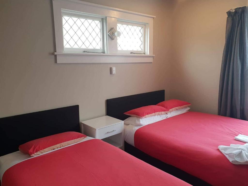 two beds in a room with red sheets and a window at Gretna Hotel Taihape in Taihape