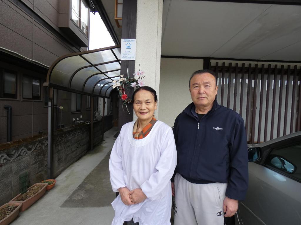 Ein Mann und eine Frau stehen neben einem Auto in der Unterkunft Minpaku Suzuki in Hiraizumi