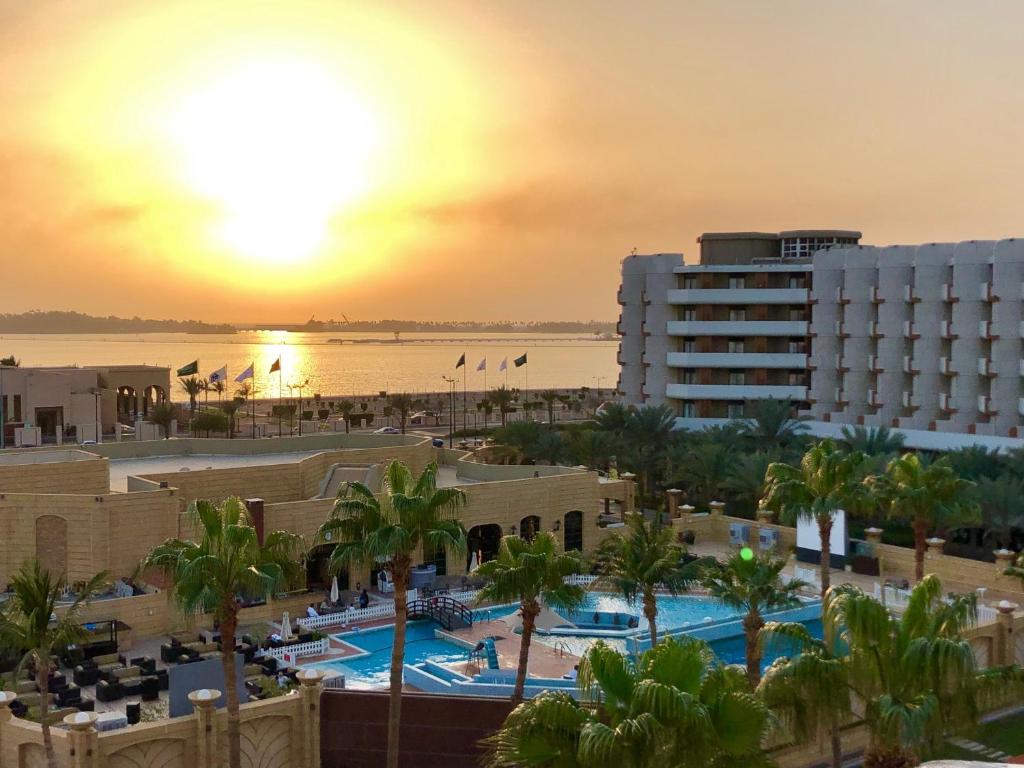a sunset over a resort with a pool and a beach at The Apartments in Jeddah