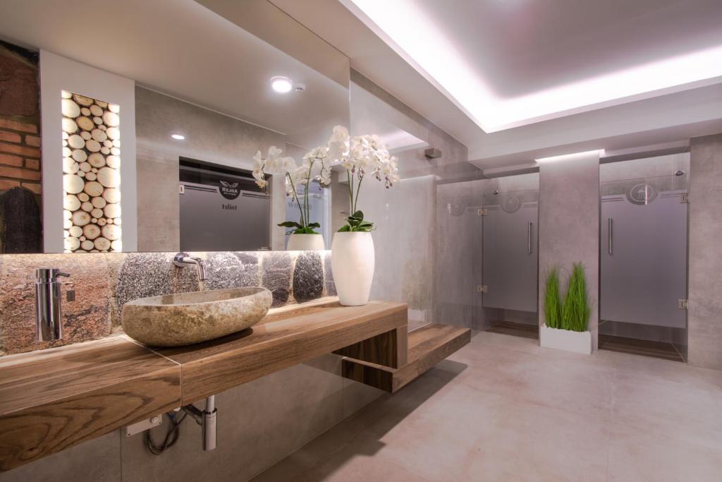 Stone basin sink on floating wooden counter, orchid vase, large mirror, and frosted stalls.