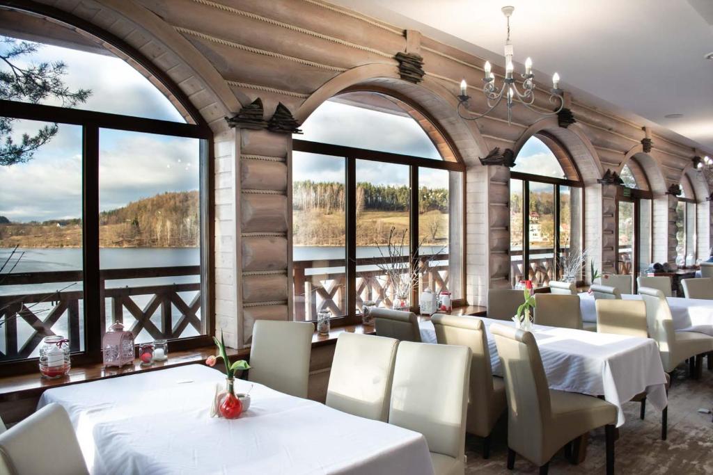 Dining room with white-clothed tables, arched windows framing tranquil lakeside views.