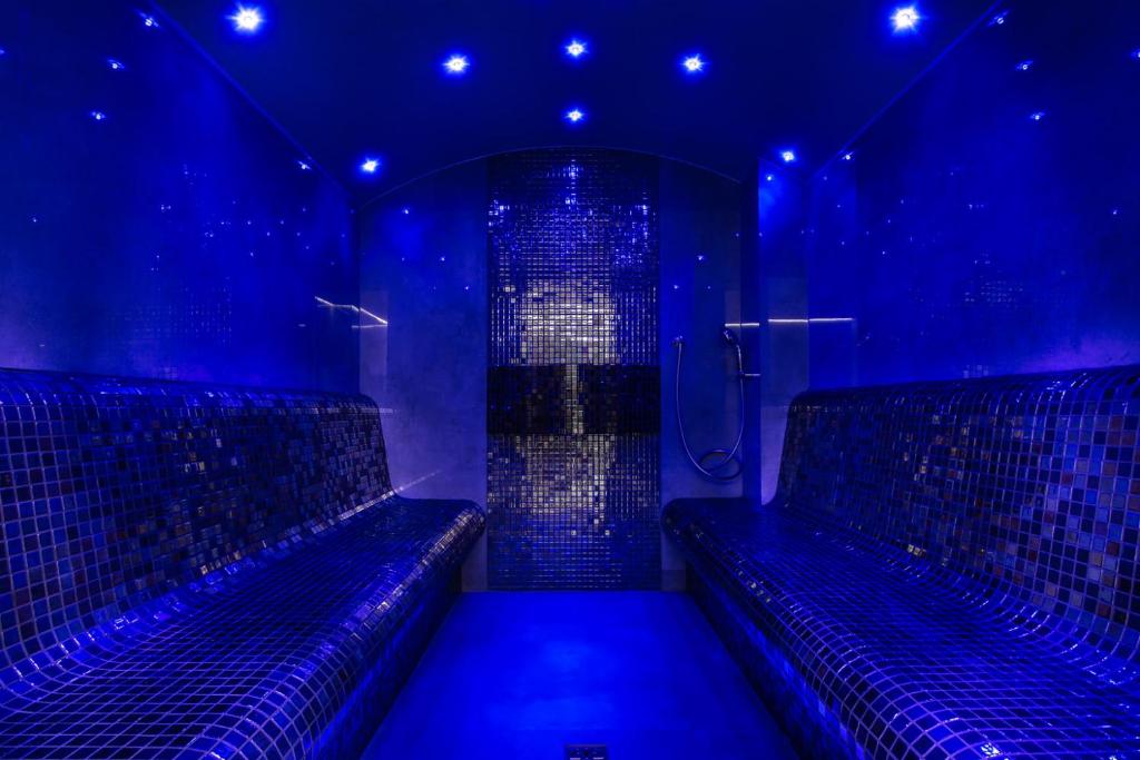 Dim steam room with mosaic-tiled curved benches and star-like blue LED lighting.