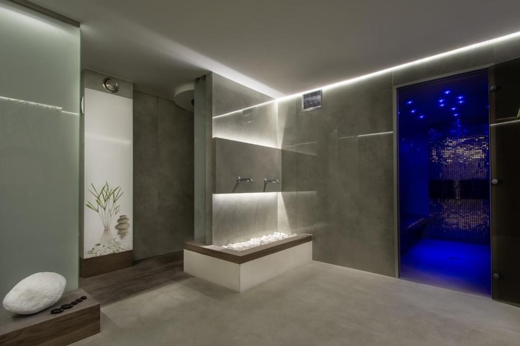 Minimalist spa room with stone-filled bench, wall faucets, and blue-lit steam room entrance.