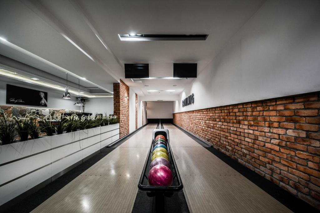 Single bowling lane with colorful balls on rack, modern interior, brick wall and plants.