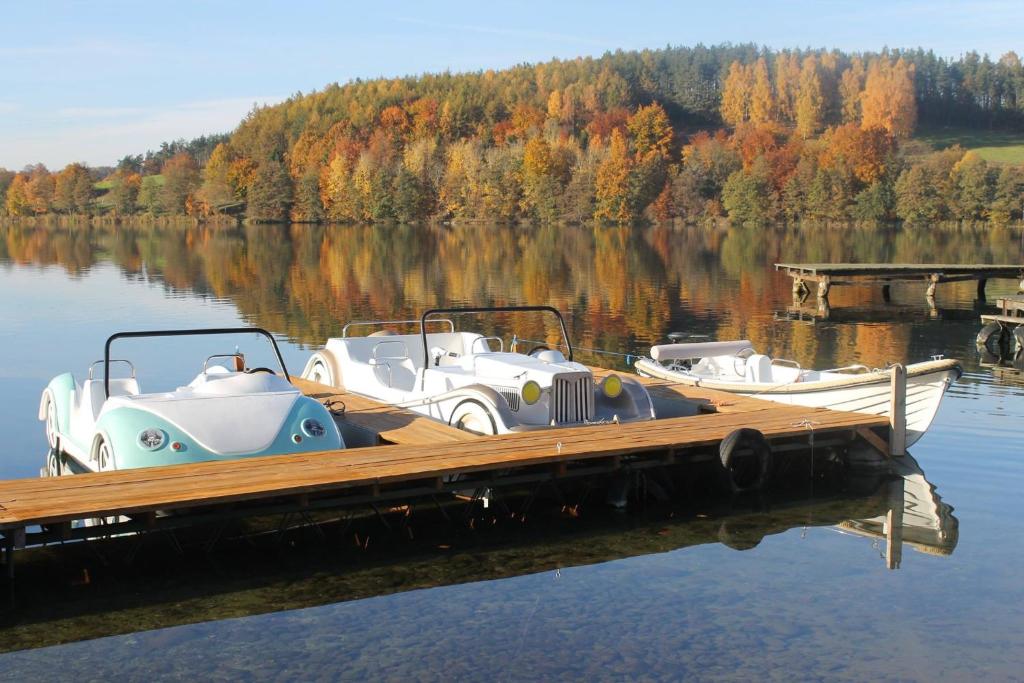 Three vintage-style pedal boats moored at wooden pier, autumn trees reflected in lake.