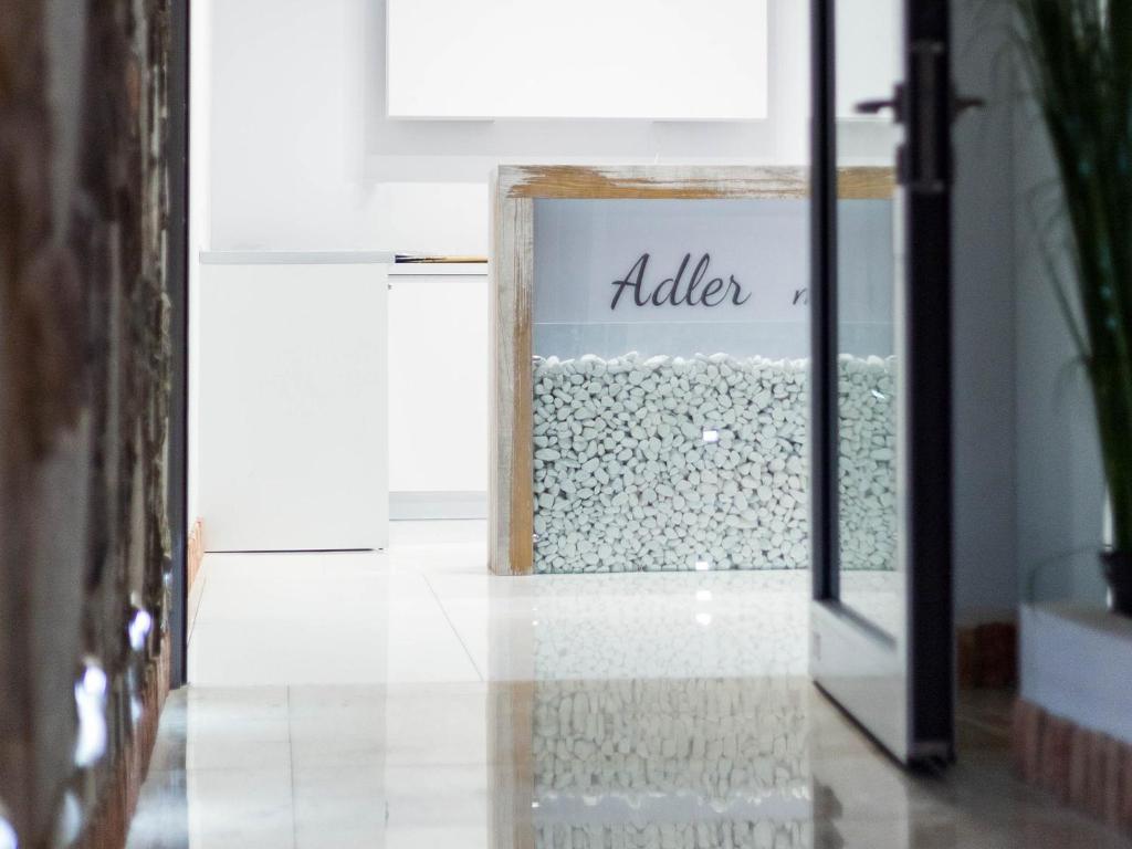 Minimal white reception hallway seen through doorway, glass panel of white stones, partial 'Adler' text.