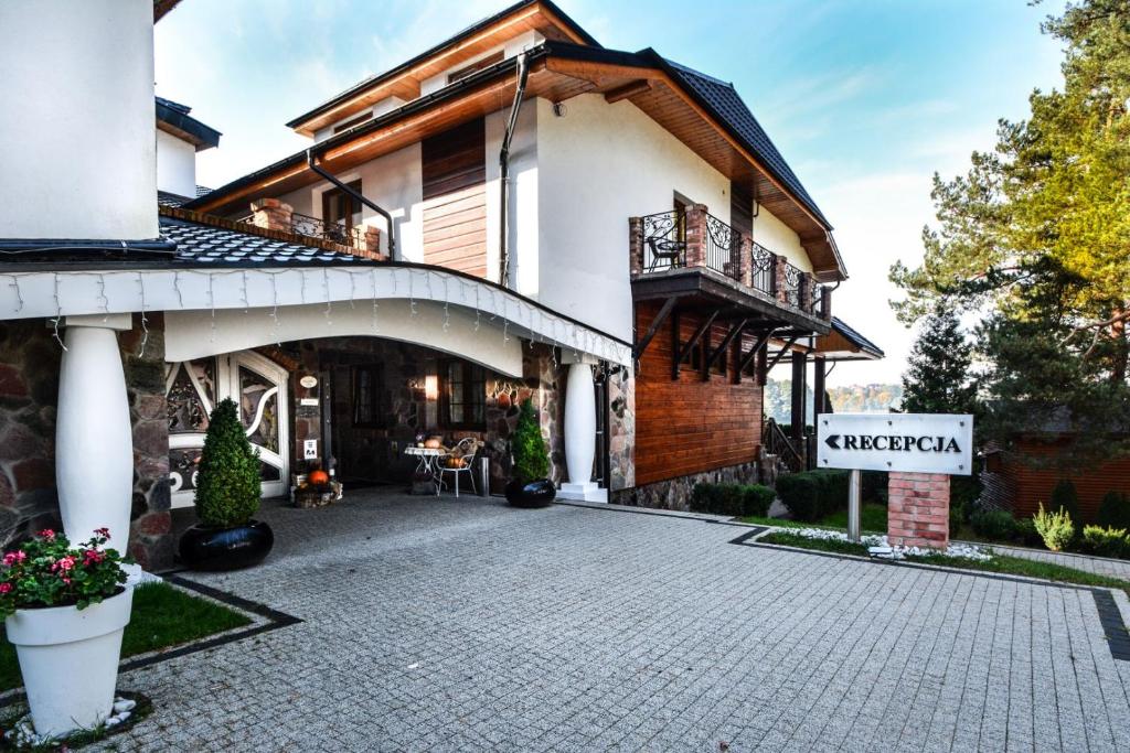 Entrance of lakeside lodge with covered porte-cochere, potted plants, 'Recepcja' sign pointing right.