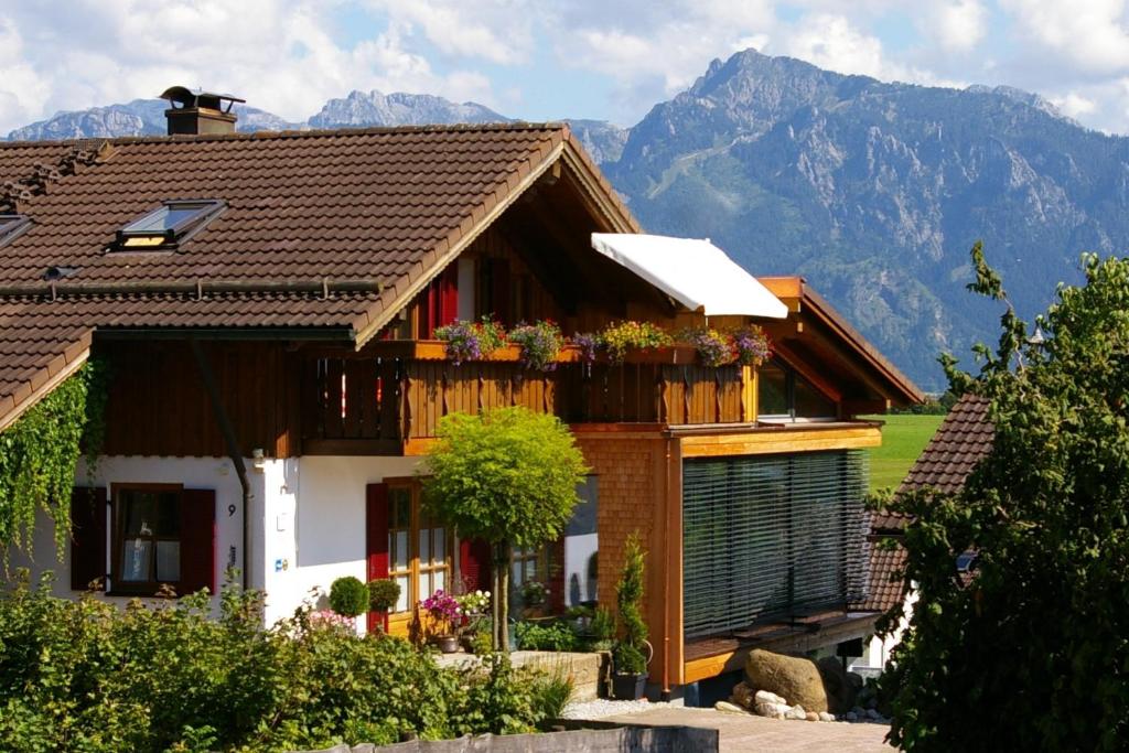 a house with flowers on a balcony with mountains in the background at Haus Bergblick in Rieden am Forggensee