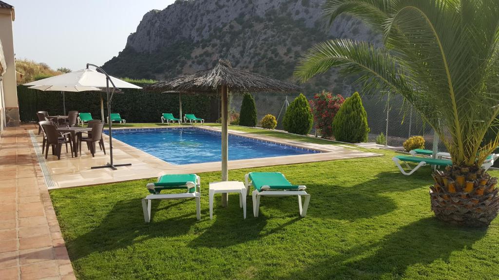einen Hinterhof mit einem Pool mit Stühlen und einem Sonnenschirm in der Unterkunft Casitas Cueva del Gato in Benaoján