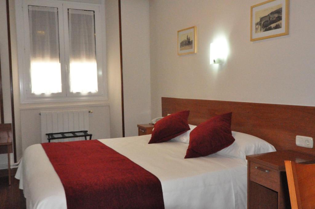 a bedroom with a bed with red pillows and a window at Pension Alameda in San Sebastián